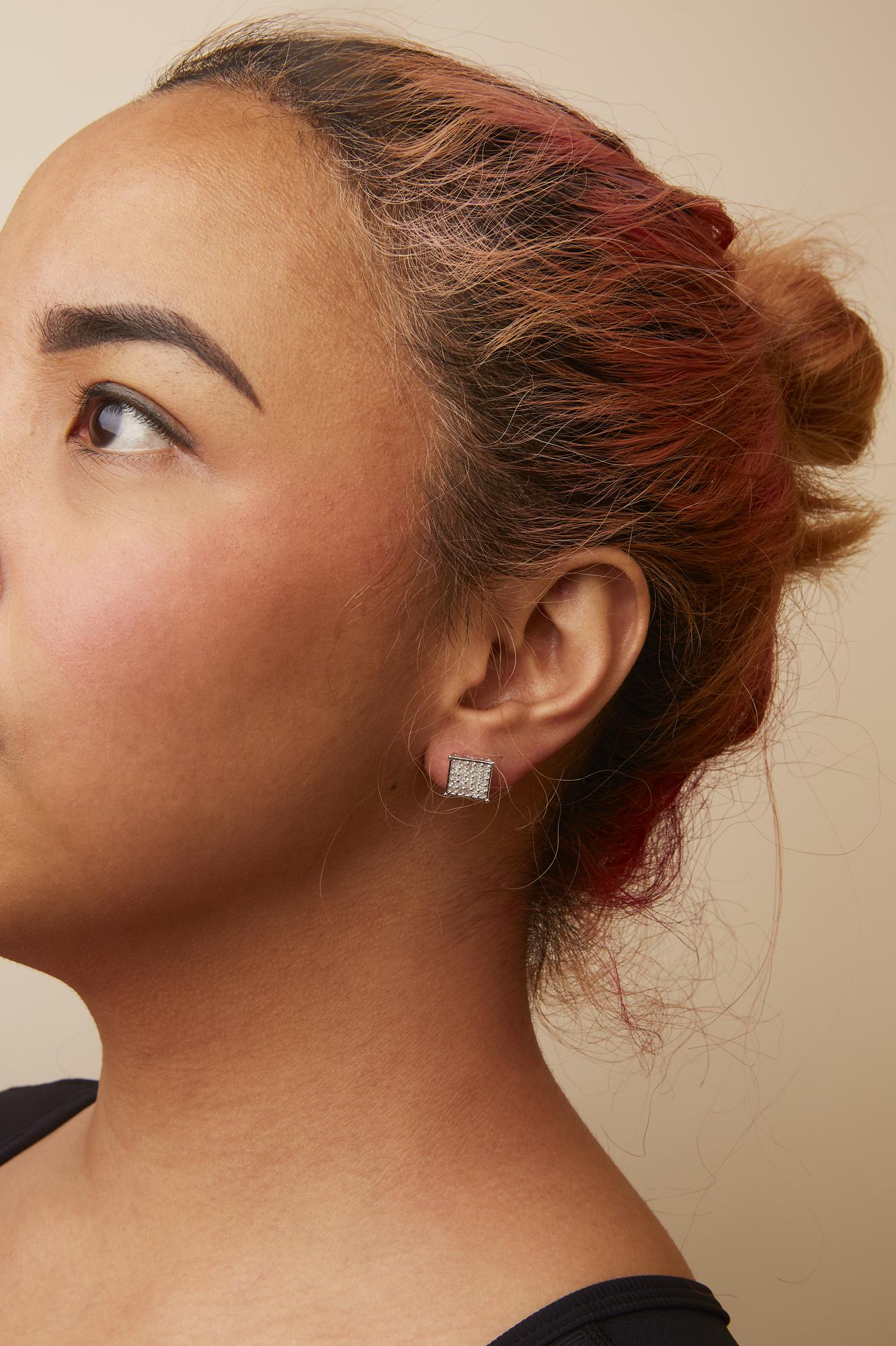Close-up side view of a model wearing square-shaped white metal stud earrings with multiple small white gemstones in prong settings.