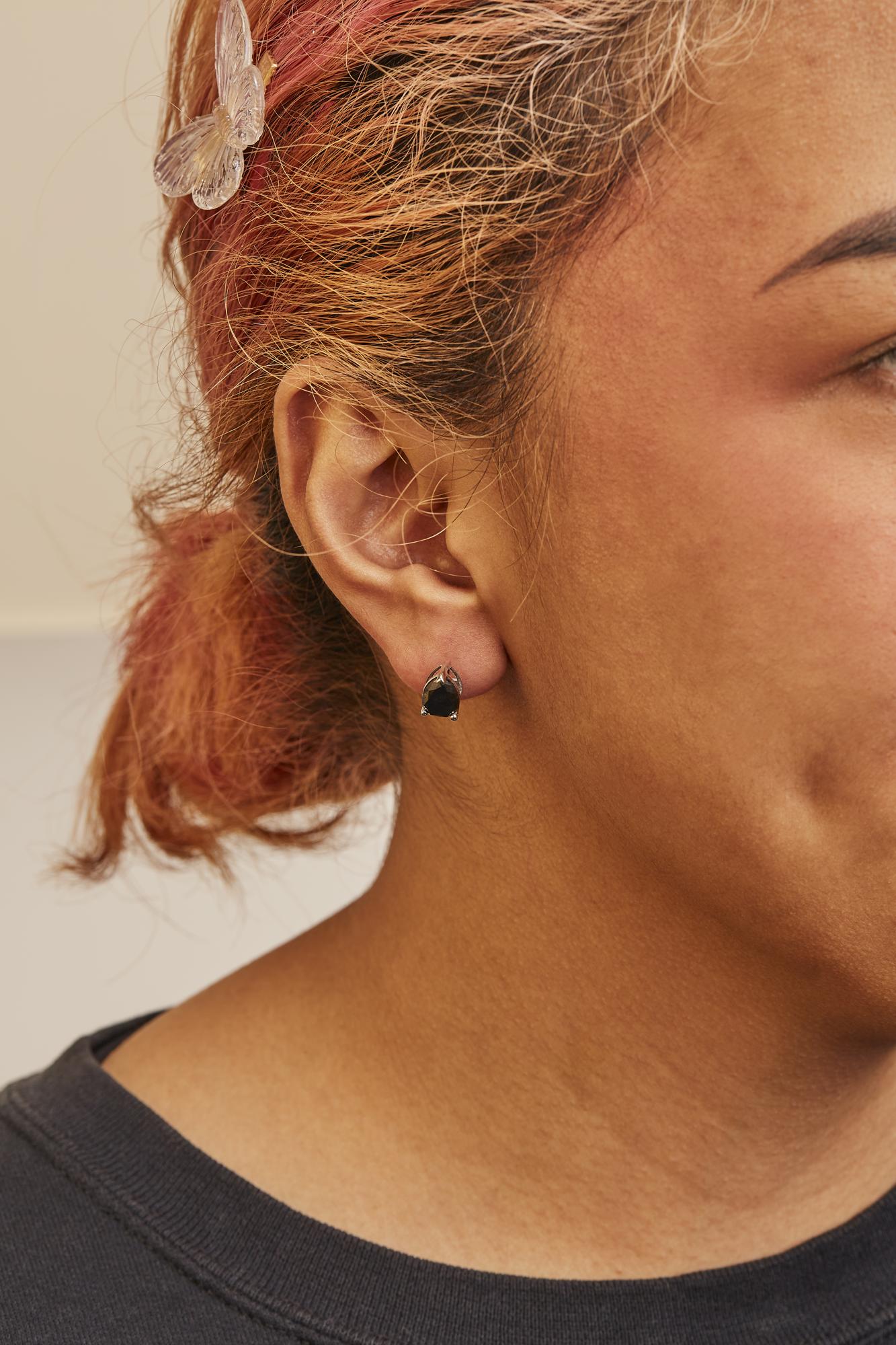 Close-up side view of a model wearing a pair of white metal earrings featuring pear-shaped black gemstones in a prong setting.