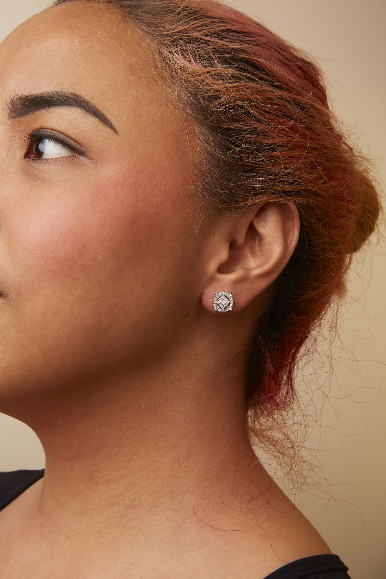 Close-up side view of a model wearing square-shaped white metal stud earrings featuring a cluster of white round and princess-shaped gemstones in prong and invisible settings.