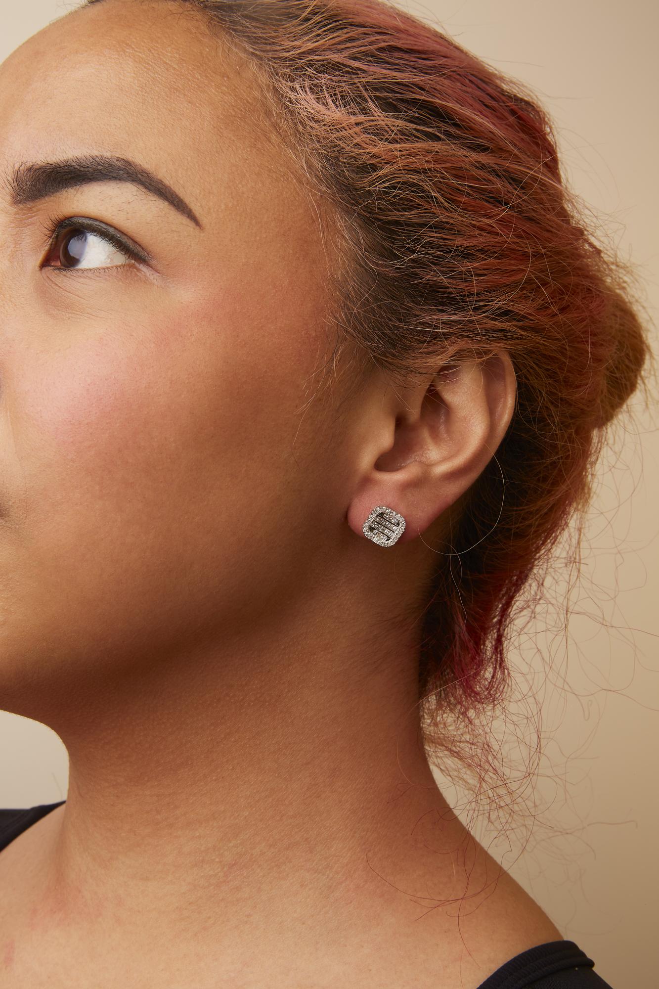 White metal stud earrings with princess and round white gemstones, worn on a model, shown in a close-up side view.