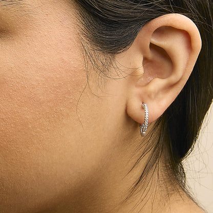 Close-up side view of a white metal hoop earring with prong-set white princess-shaped gemstones worn on a model's ear.