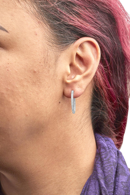 Close-up side view of a white metal hoop earring with multiple white princess-cut gemstones in prong settings, worn on a model's ear.
