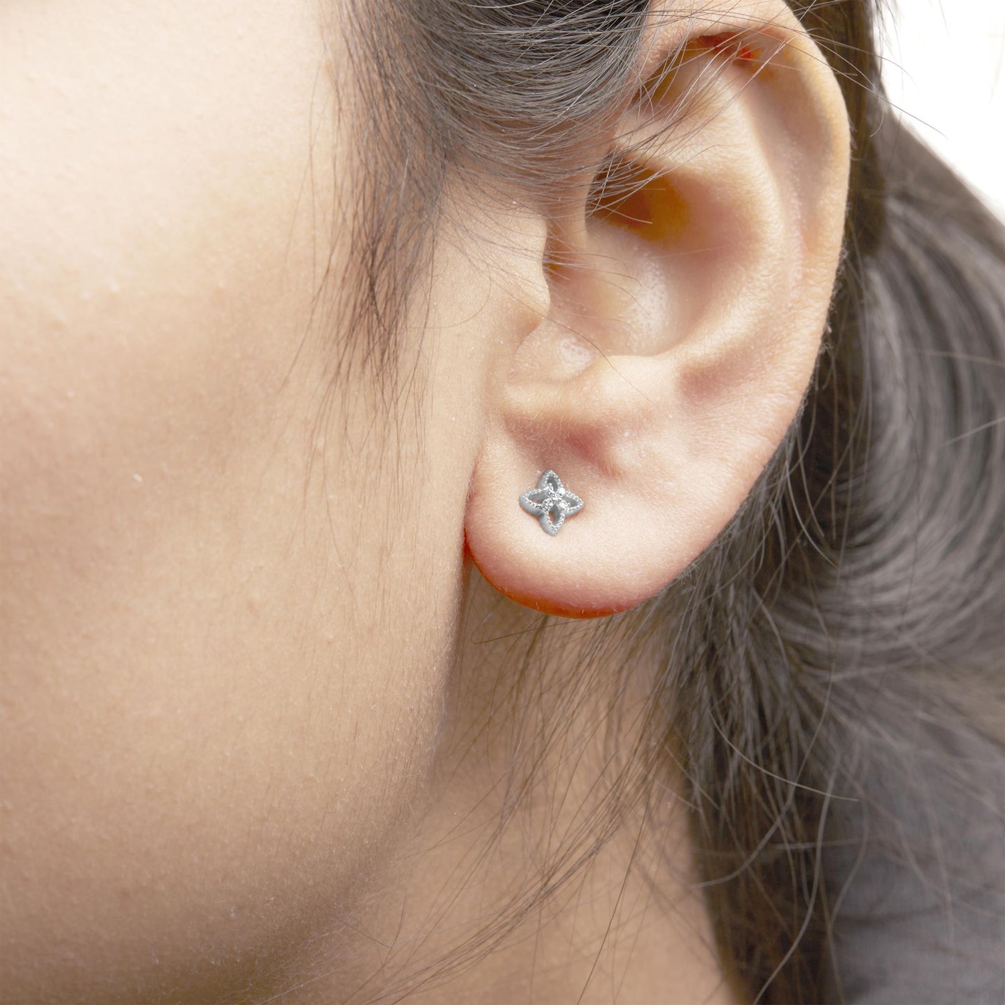 Close-up side angle of a white metal earring with a floral design featuring small round white gemstones worn on a model's ear.