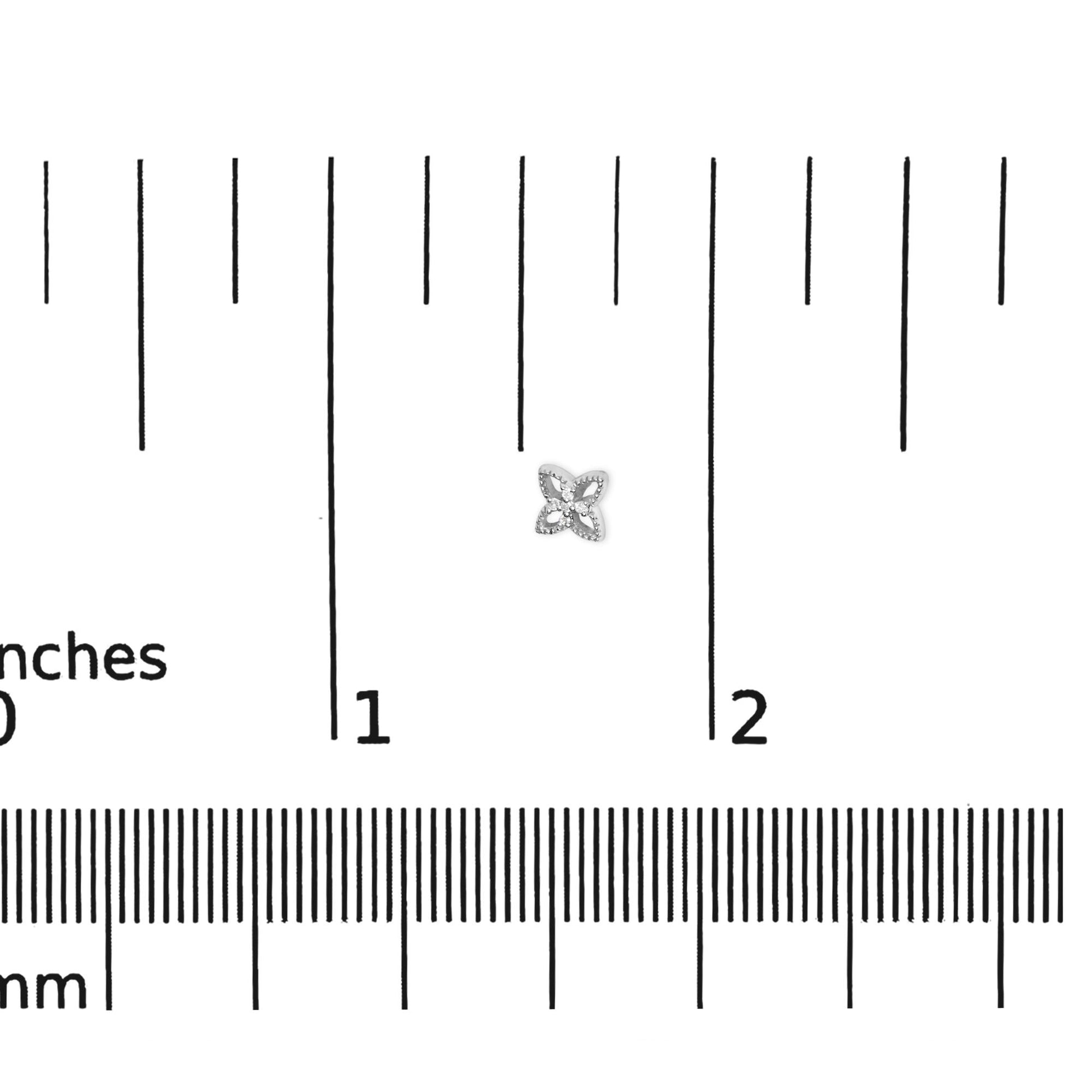 White metal stud earring with round white gemstones in prong setting, flower-like shape, shown on a ruler for size reference, top-down angle.