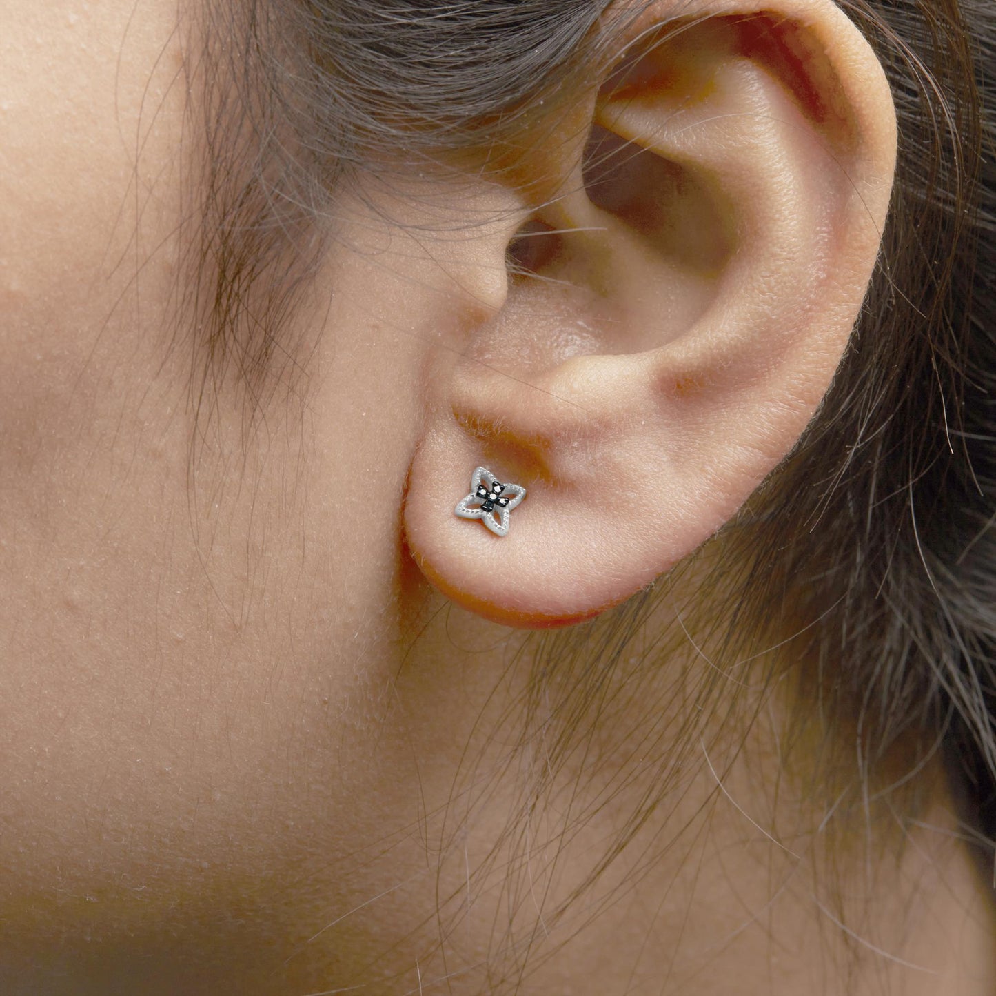 Close-up side view of a white metal stud earring on a model's ear, shaped like a four-petal flower with round blue gemstones in prong settings.