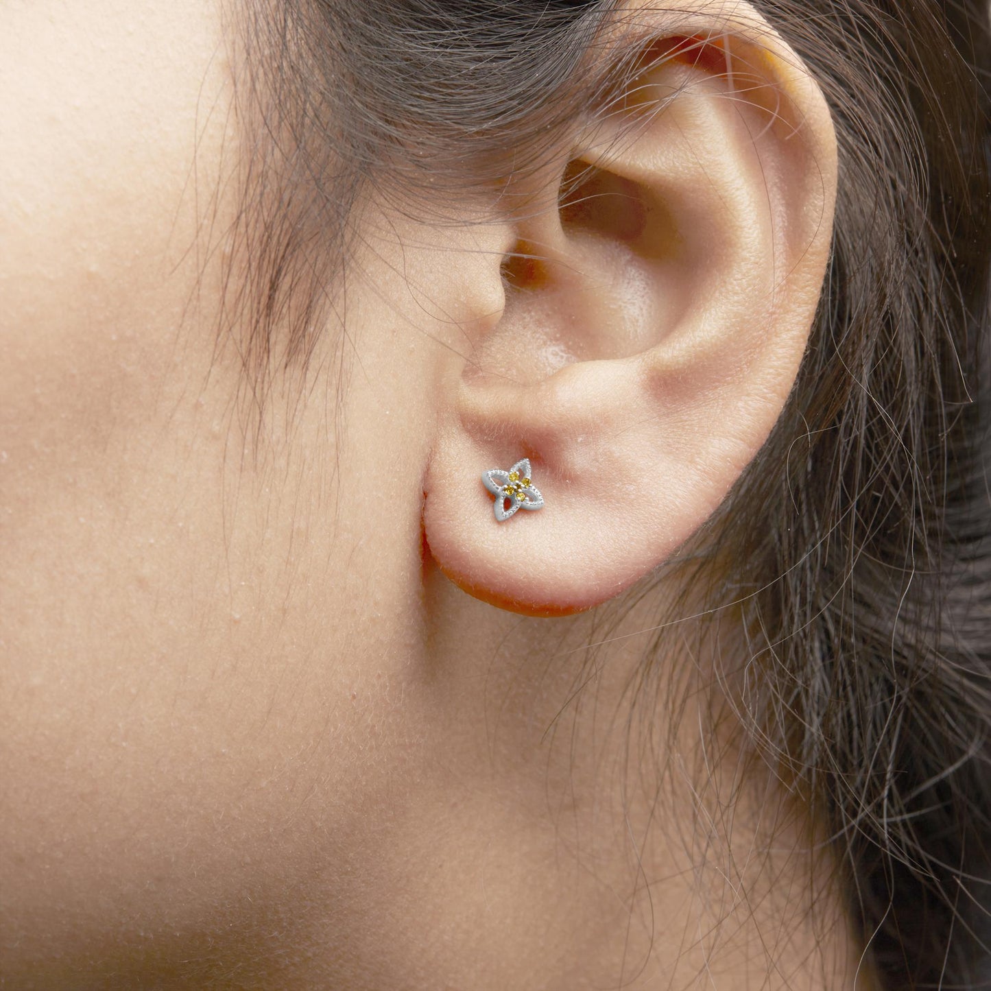 Close-up side angle of a white metal earring on a model's ear featuring a floral design with small yellow round gemstones in a prong setting.