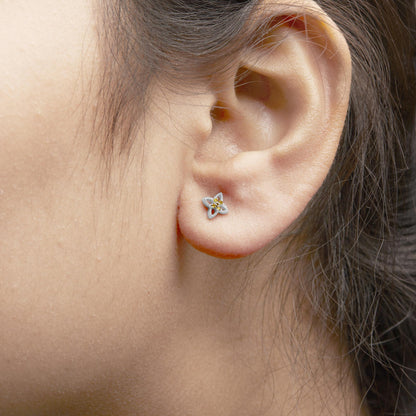 Close-up side angle of a white metal earring on a model's ear featuring a floral design with small yellow round gemstones in a prong setting.