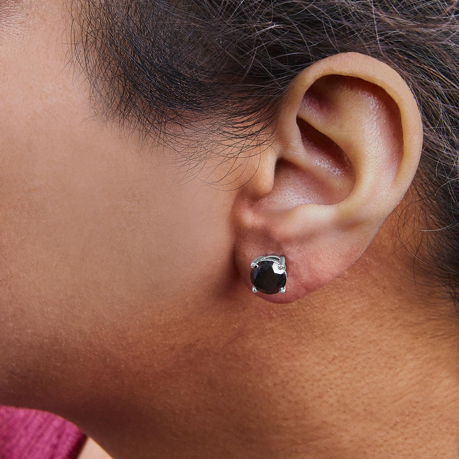 Close-up side view of a white metal earring with a round black gemstone in a 4-prong setting worn on a model's ear.