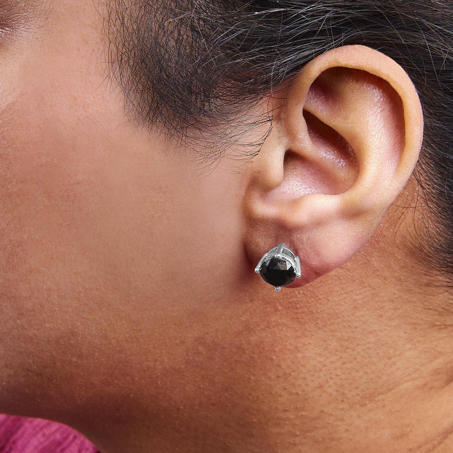 Close-up side view of an ear wearing a white metal stud earring with a round black gemstone in a four-prong setting.