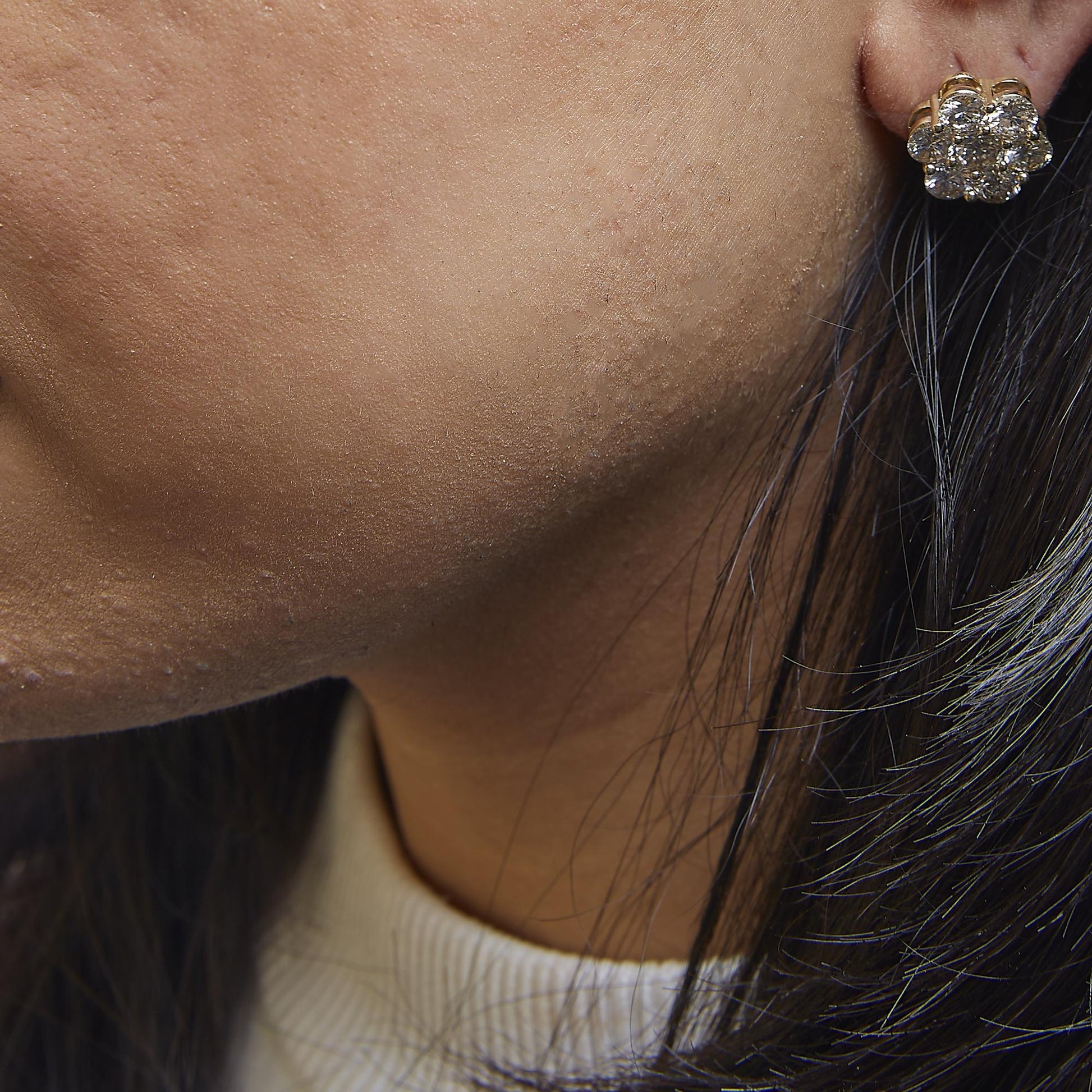 Close-up side view of a yellow metal cluster earring with multiple round white gemstones on a model.