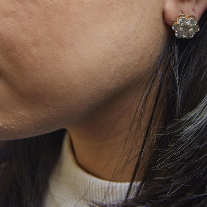 Close-up side view of a yellow metal cluster earring with multiple round white gemstones on a model.