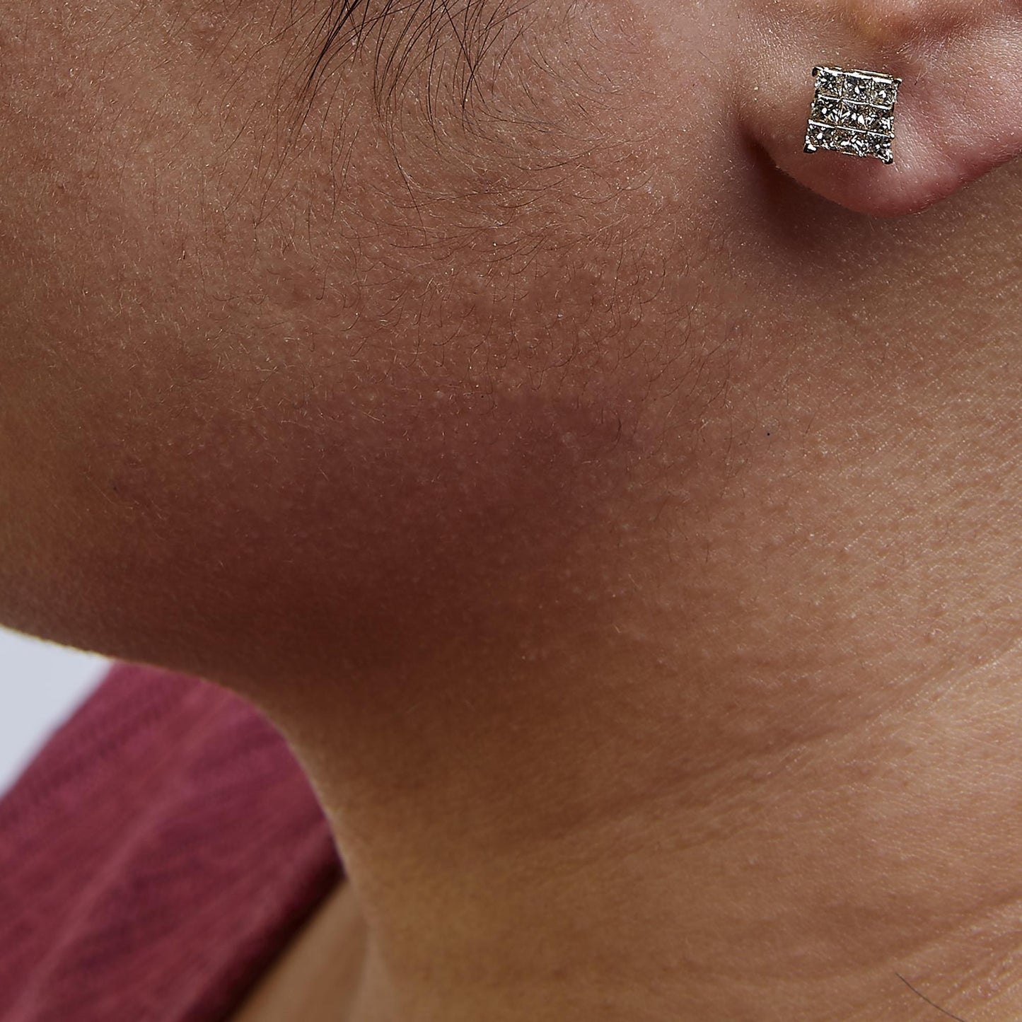 Close-up side view of a model wearing yellow metal square-shaped stud earrings set with multiple princess-cut white gemstones in an invisible setting.