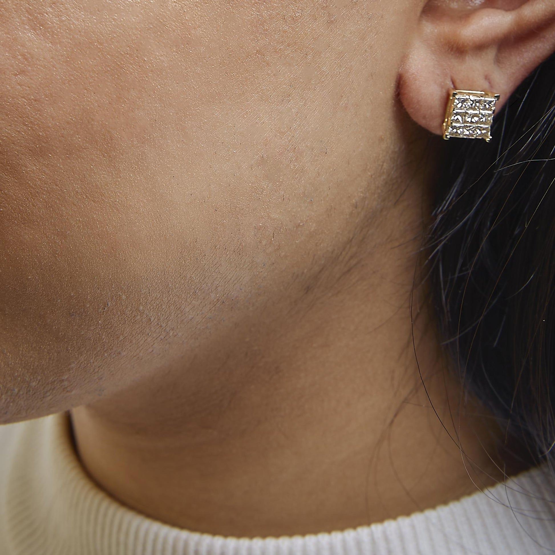 Close-up side view of a yellow metal square-shaped earring with white princess-shaped gemstones in an invisible setting, worn on a model.