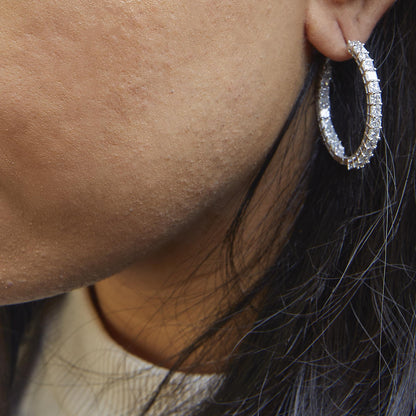 Close-up side view of a white metal hoop earring on a model’s ear, featuring two rows of shared prong-set princess-shaped white gemstones.