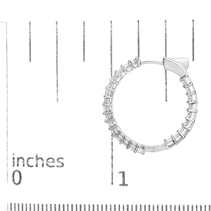Close-up front angle of a white metal hoop earring with shared prong settings holding white princess shape gemstones, placed on a ruler for size reference.