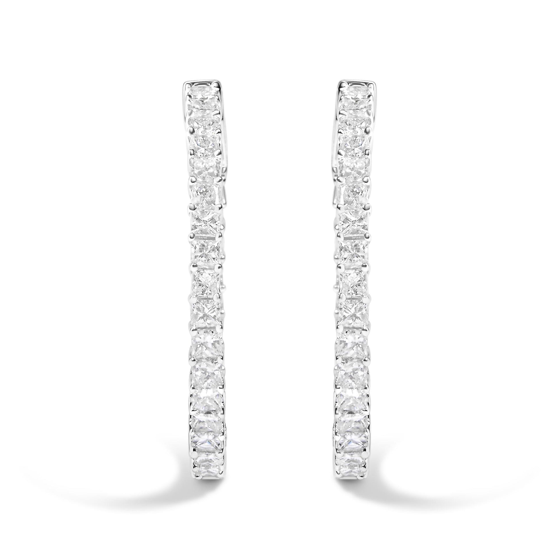 Front angle close-up of a pair of white metal hoop earrings set with square and round white gemstones in a shared prong setting.