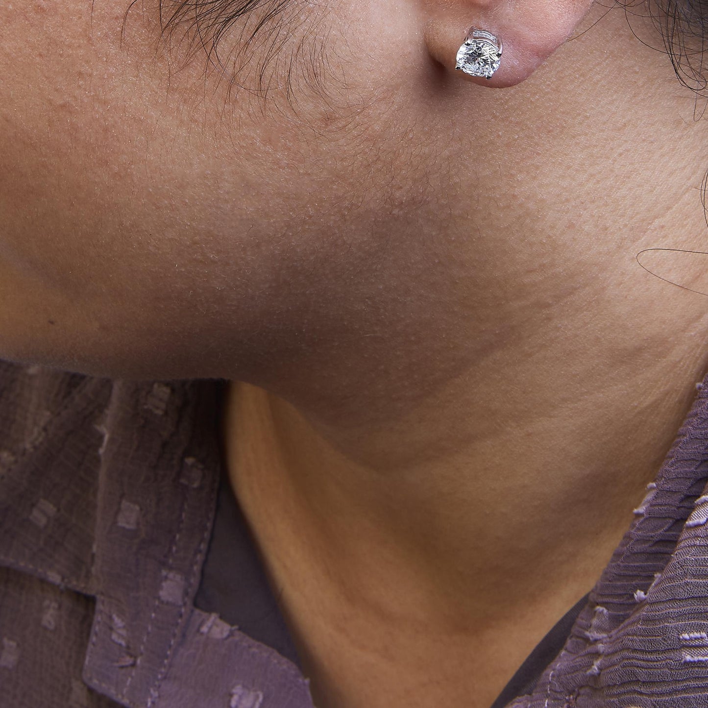 Close-up side view of a white metal stud earring with a round white gemstone in a 4-prong setting, worn on a model.