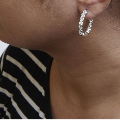 Close-up side view of a model wearing a white metal hoop earring set with round white gemstones in a shared prong setting.