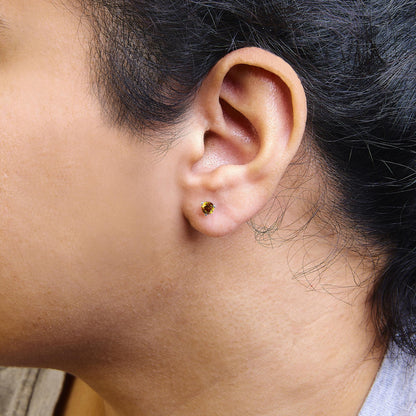 Close-up side view of white metal stud earring with round orange gemstone in 3-prong setting, worn on a model's ear.