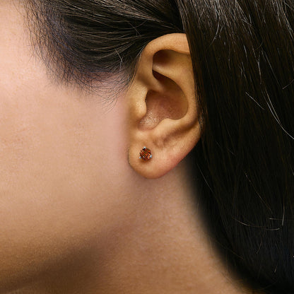 Close-up side view of a white metal stud earring with a round red gemstone in a three-prong setting, shown worn on a model's ear.