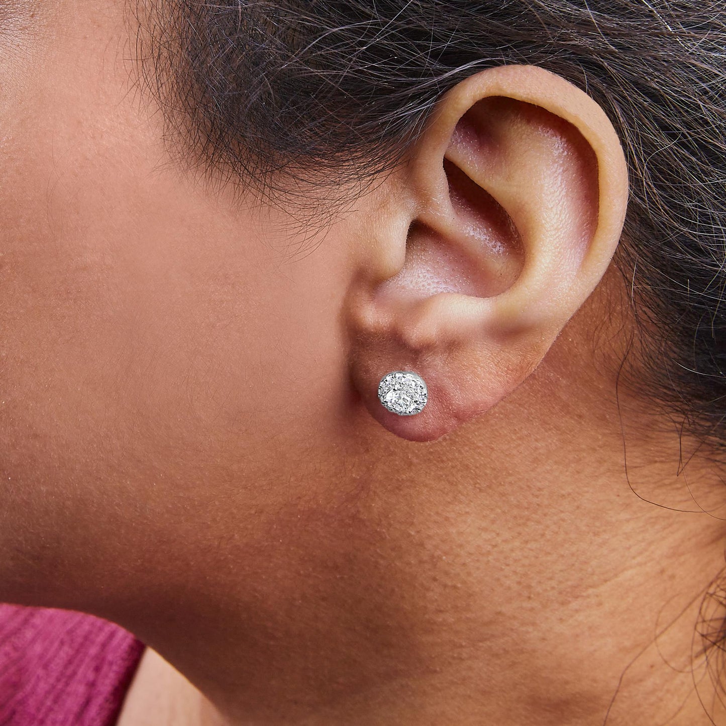 Close-up side view of a white metal stud earring with multiple round white gemstones in prong settings, worn on a model.