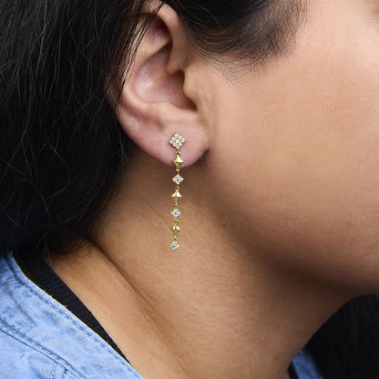 Close-up side view of a yellow metal drop earring on a model's ear, featuring multiple round white gemstones in prong settings.