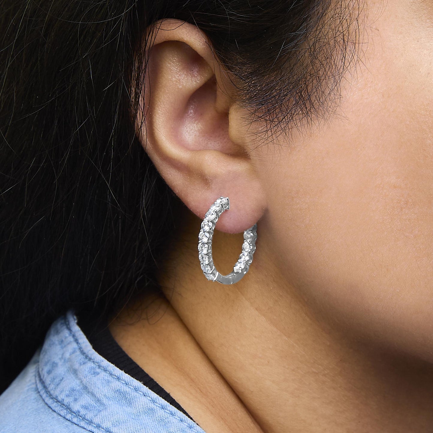Close-up side view of a white metal hoop earring set with round white gemstones in shared prong settings, worn on a model.