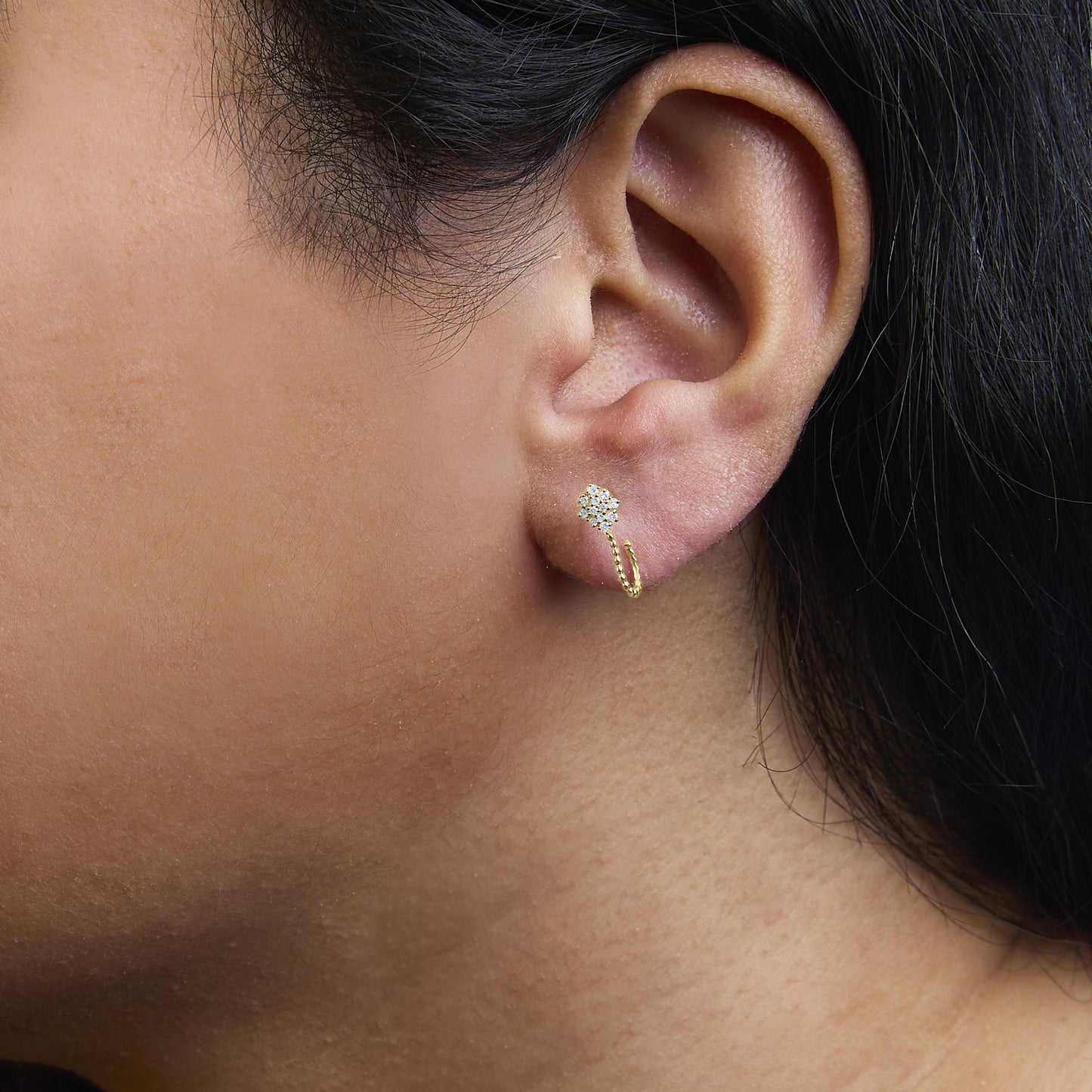 Close-up side view of a yellow metal earring with cluster of round white gemstones in prong setting, worn on a model.