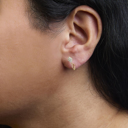 Close-up side view of a yellow metal earring with cluster of round white gemstones in prong setting, worn on a model.