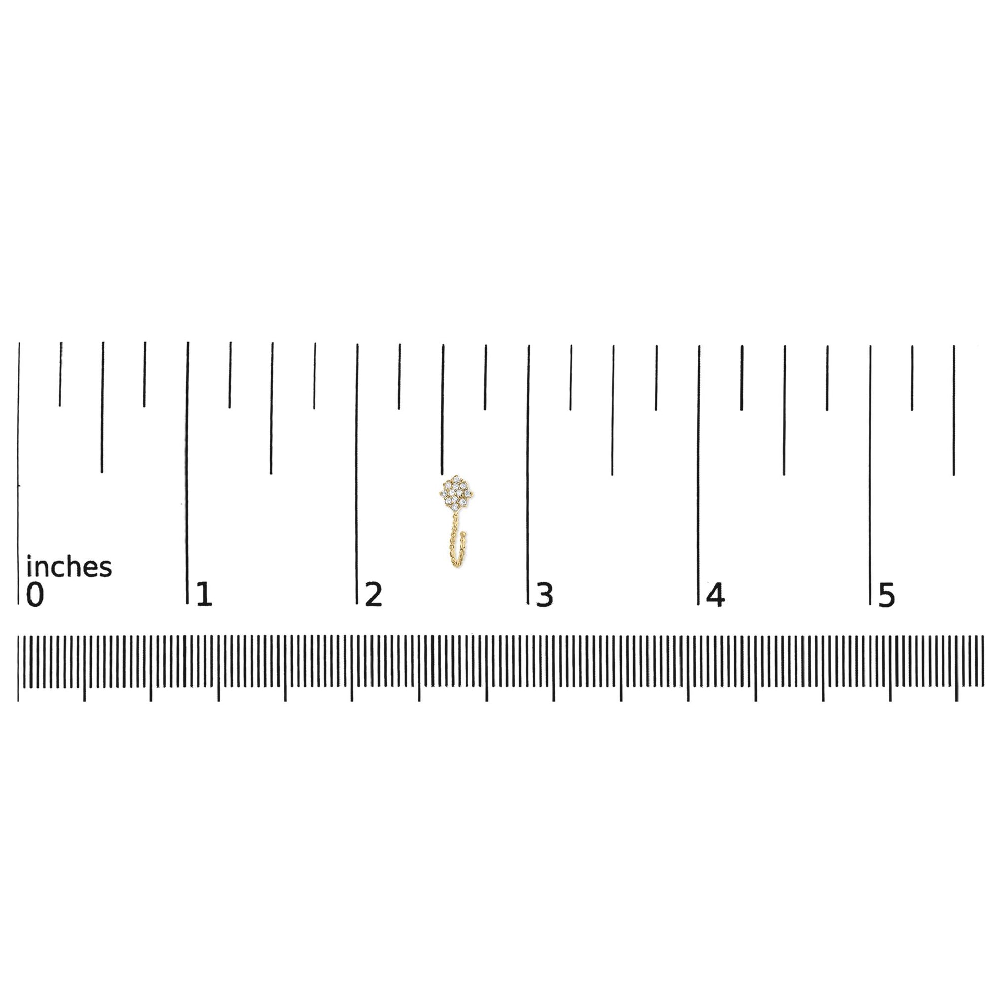 Small yellow metal earring with round white gemstones in prong setting, shown on a ruler for size reference, top-down angle.