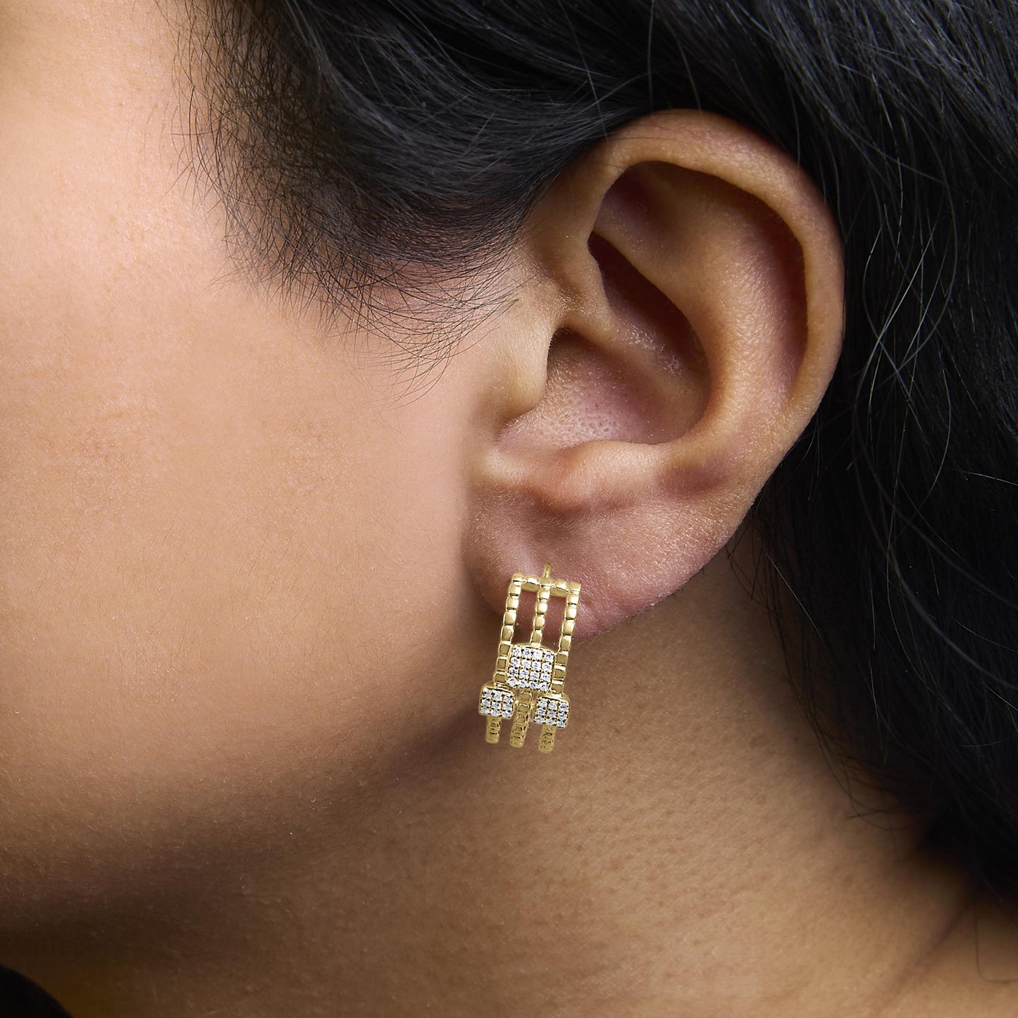 Close-up side view of an ear wearing yellow metal earrings featuring white round gemstones in a prong setting.