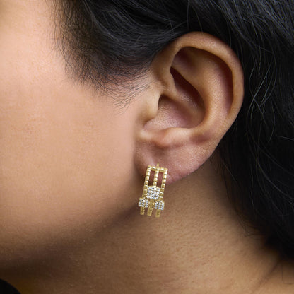 Close-up side view of an ear wearing yellow metal earrings featuring white round gemstones in a prong setting.