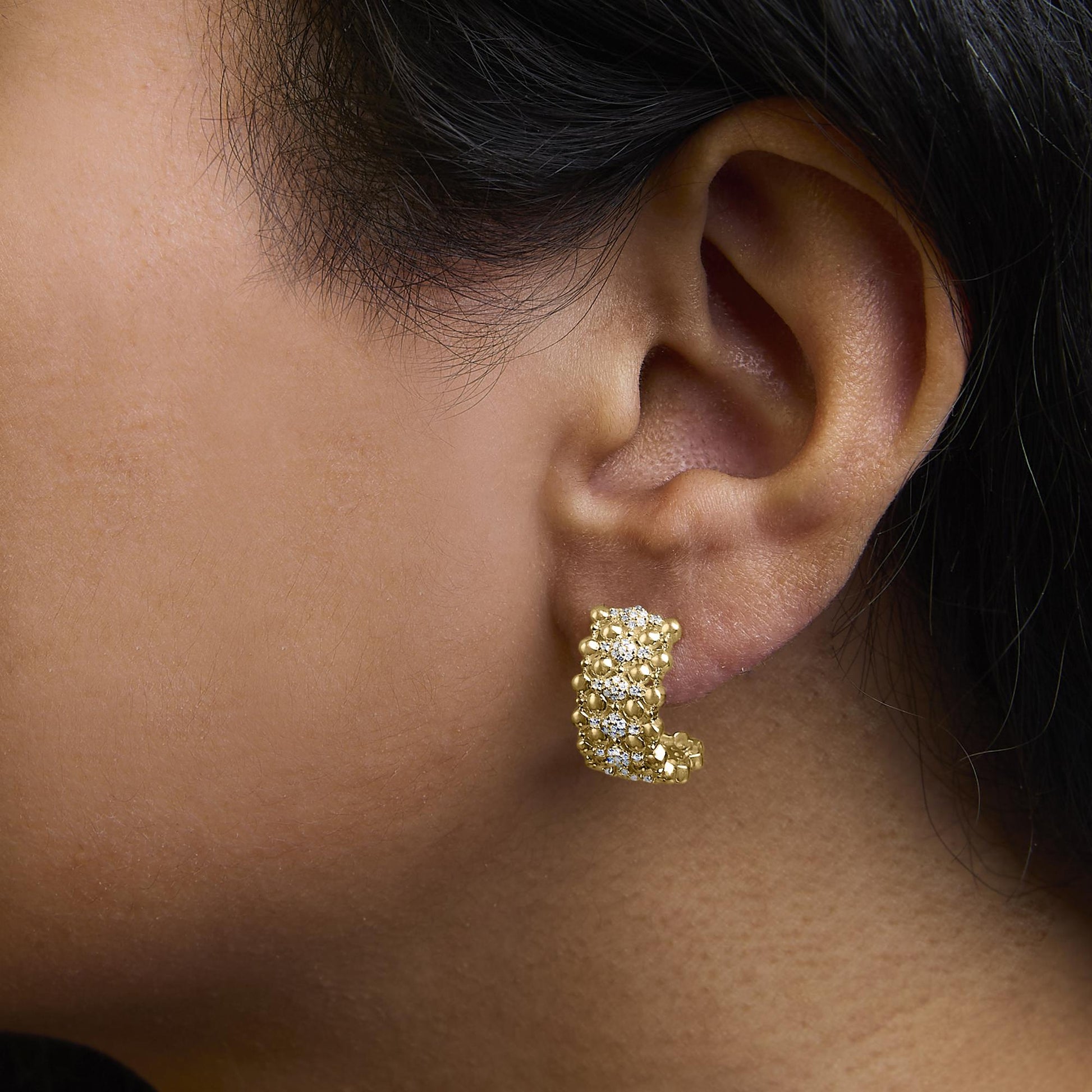 Close-up side angle of a model wearing a yellow metal earring featuring round white gemstones in prong settings.