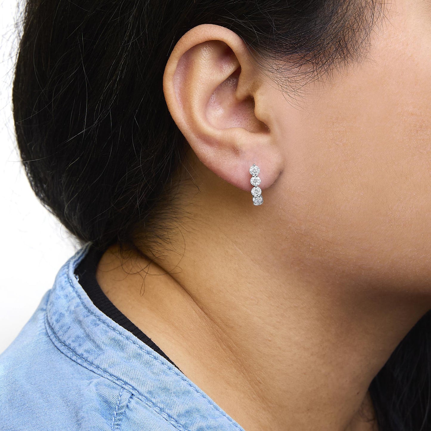 Close-up side view of a model wearing white metal earrings with vertically aligned round white gemstones in prong settings.