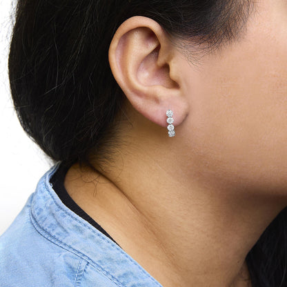 Close-up side view of a model wearing white metal earrings with vertically aligned round white gemstones in prong settings.