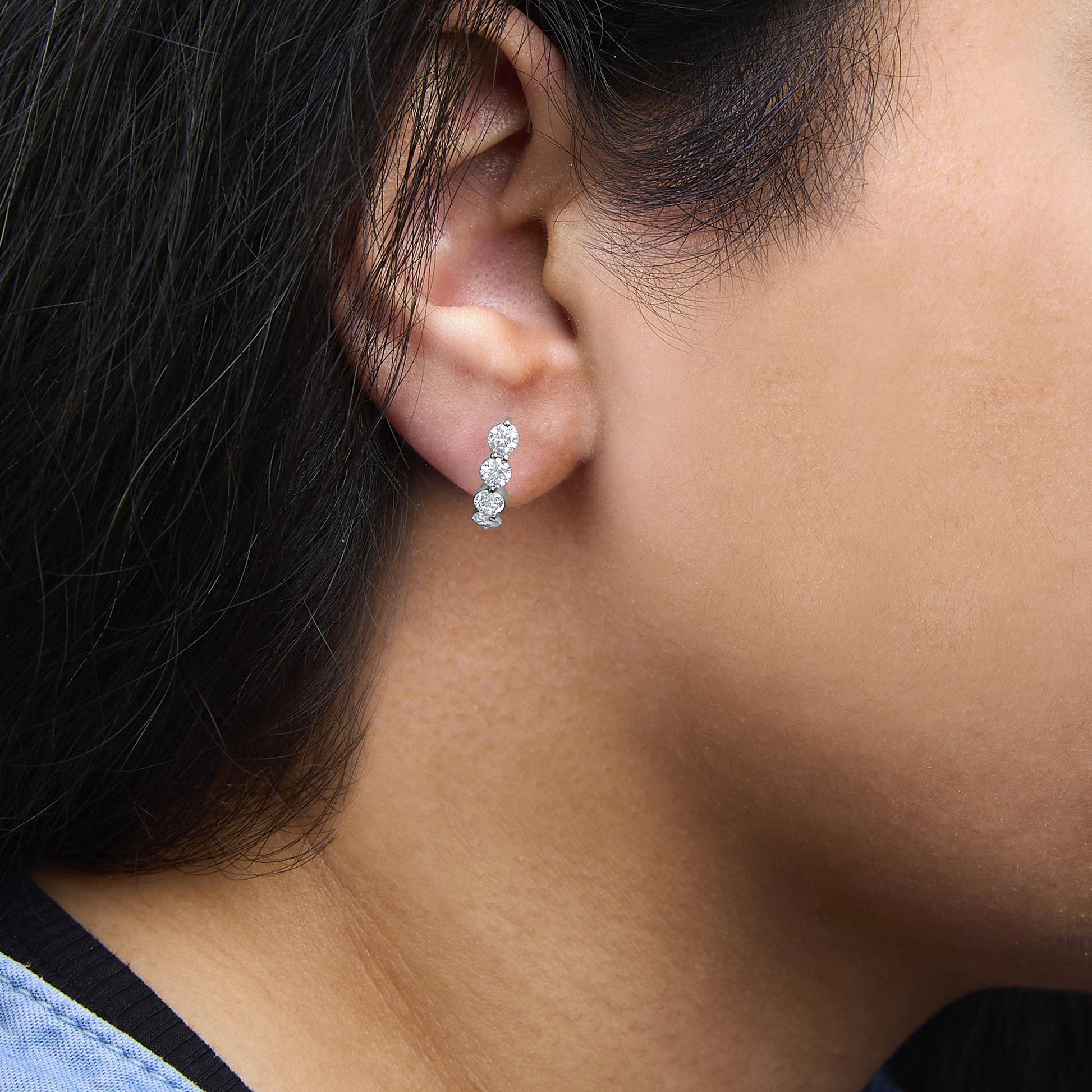 Close-up side view of white earrings with multiple round white gemstones in prong settings worn on a model's ear.