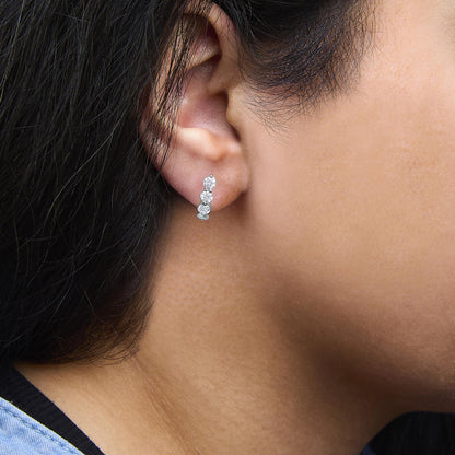 Close-up side view of white earrings with multiple round white gemstones in prong settings worn on a model's ear.