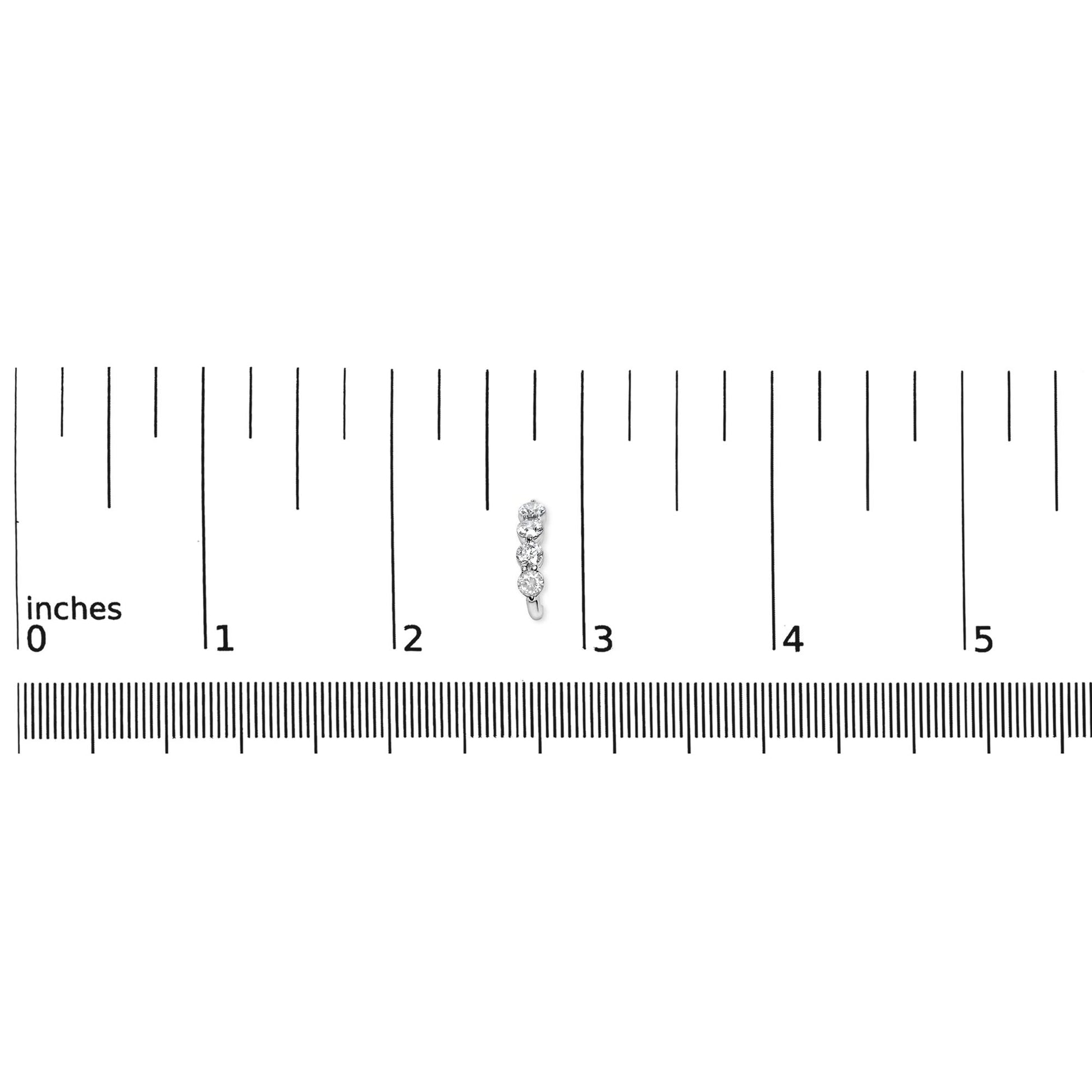 Close-up top view of a white metal earring with round white gemstones in prong settings, placed on a ruler for size reference.