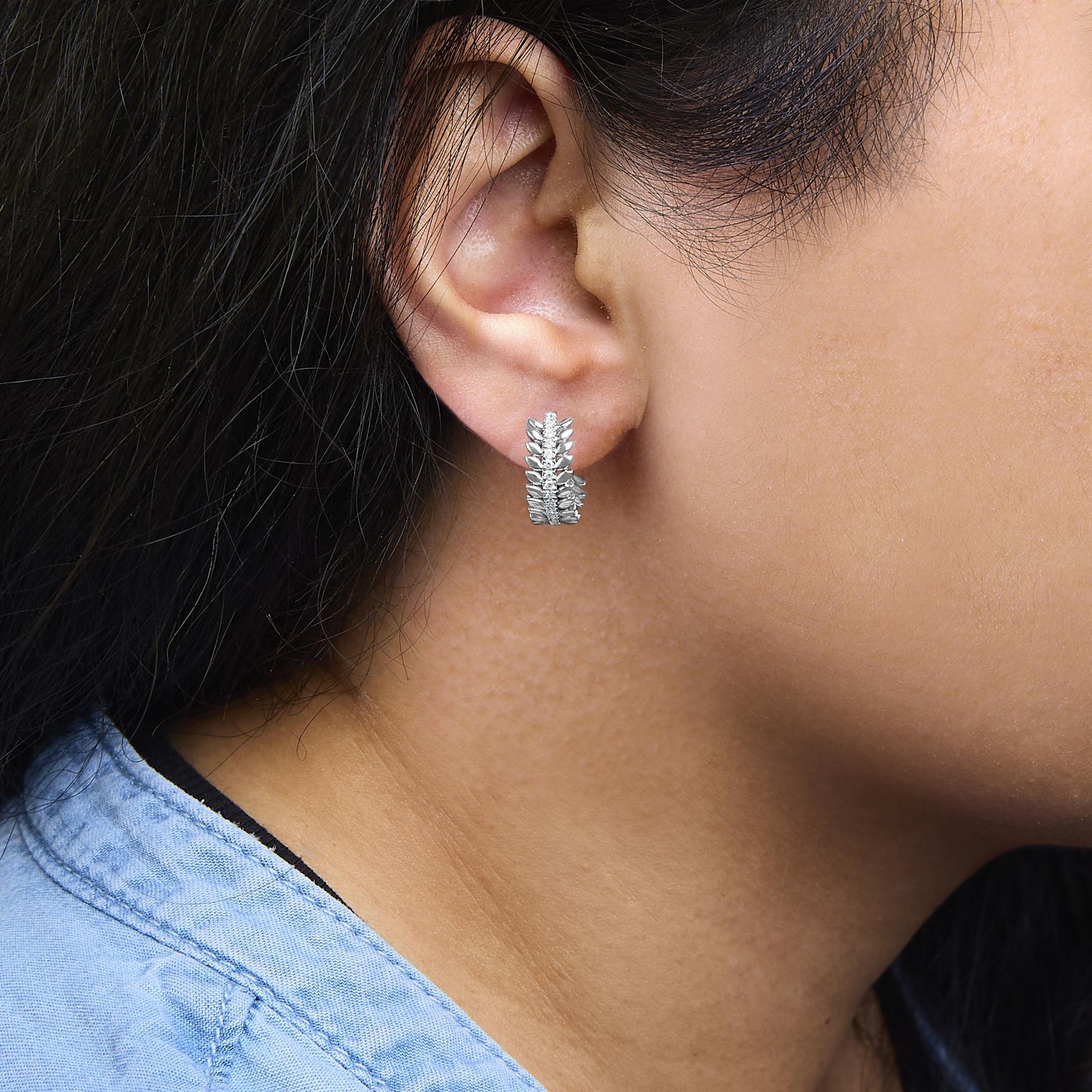 Close-up side view of a white metal earring with round prong-set white gemstones, worn on a model's ear.