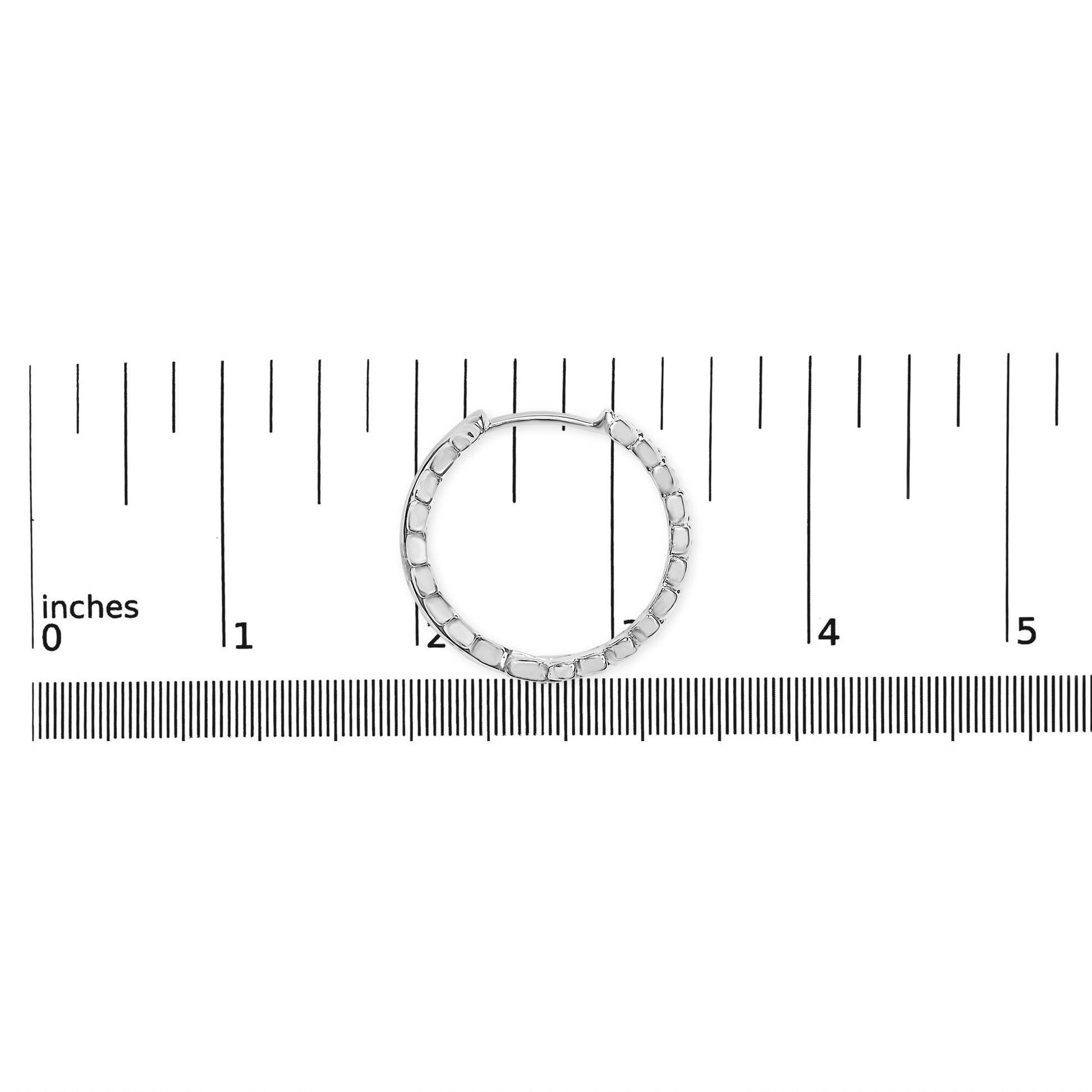 White metal hoop earring with round white gemstones in prong settings, shown flat on a ruler for size reference from a top-down angle.