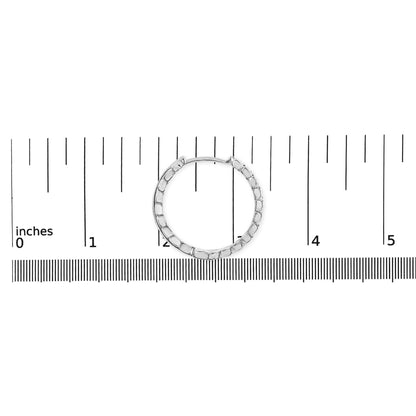 White metal hoop earring with round white gemstones in prong settings, shown flat on a ruler for size reference from a top-down angle.