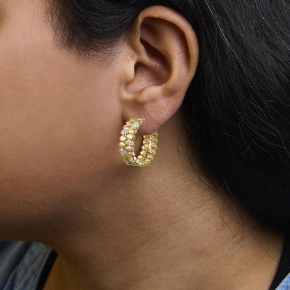 Close-up side view of a yellow metal hoop earring on a model's ear, featuring round white gemstones in prong and pave settings.