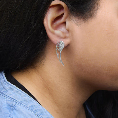 Close-up side view of a white metal earring on a model, designed with an elongated wing shape featuring multiple white gemstones in prong settings.