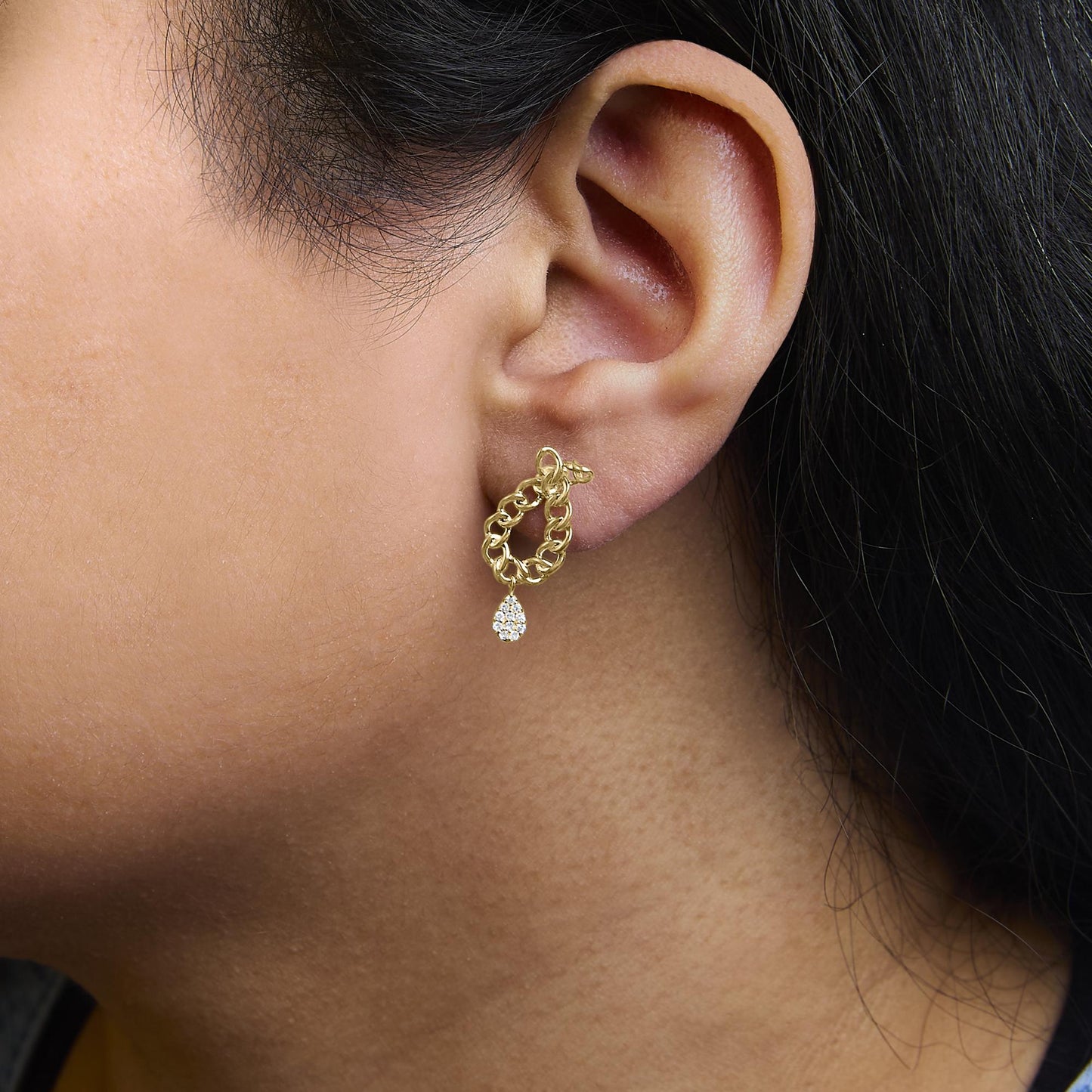 Close-up side view of a model wearing yellow metal chain-link drop earrings with a cluster of white round gemstones in a prong setting at the bottom.