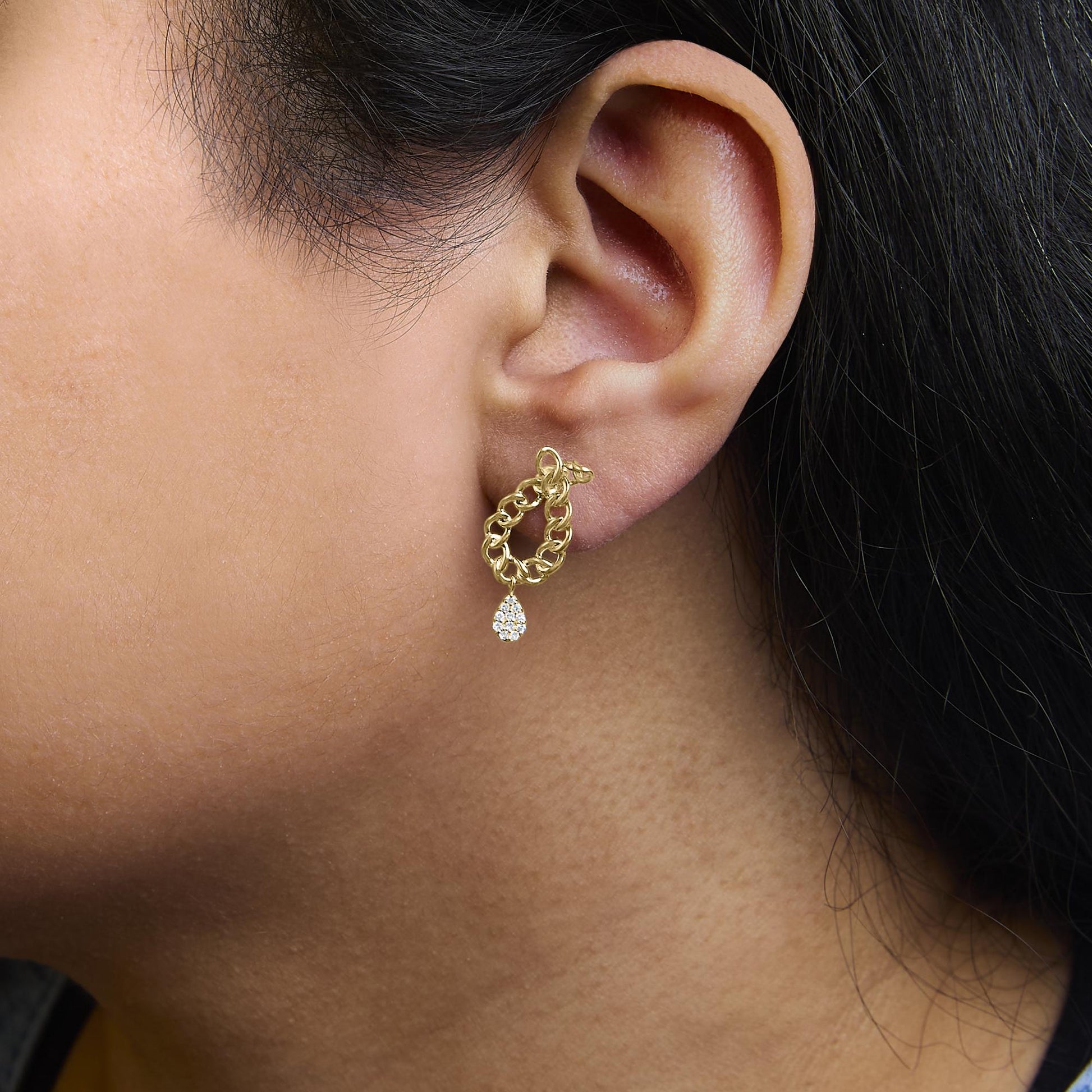 Close-up side view of a model wearing yellow metal chain-link drop earrings with a cluster of white round gemstones in a prong setting at the bottom.