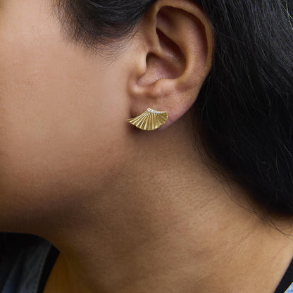 Close-up side view of a model wearing a yellow metal earring shaped like a fan with multiple small white gemstones set along the top edge.