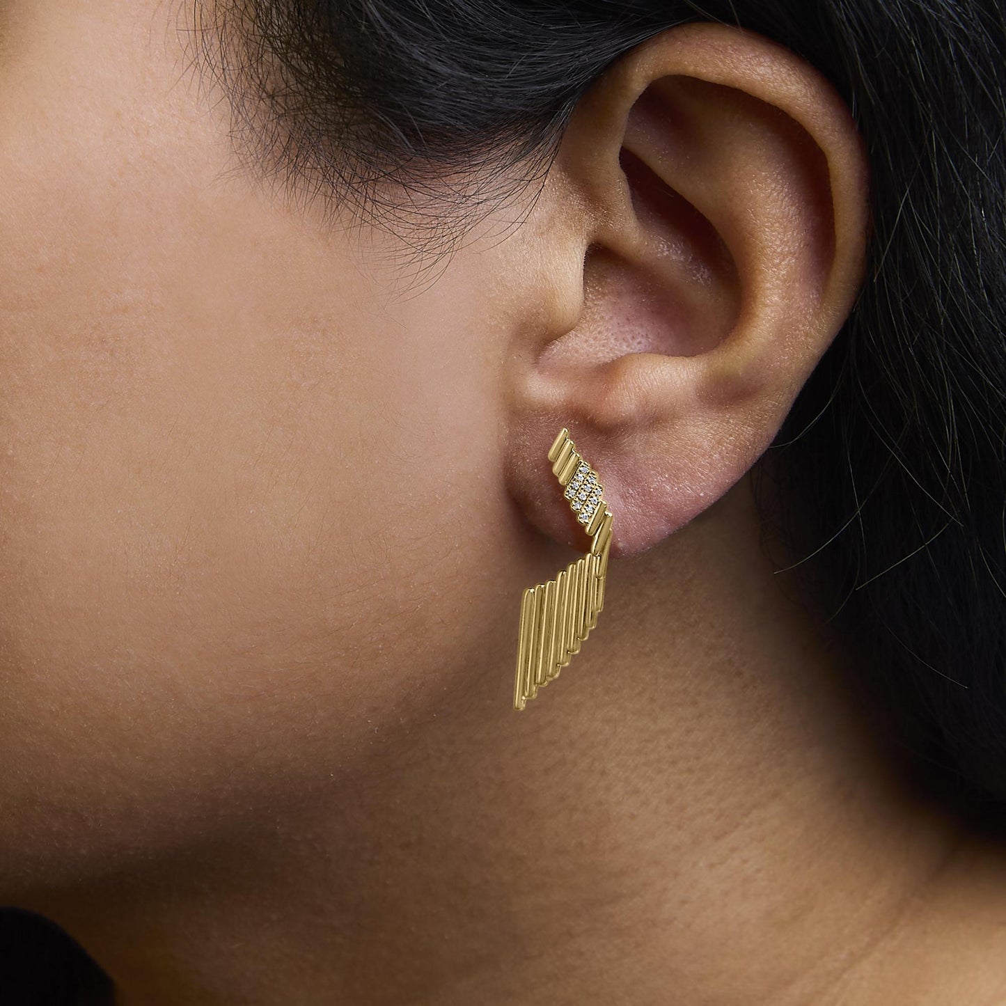 Close-up side view of a yellow metal earring with white round gemstones in prong settings, worn on a model's ear.