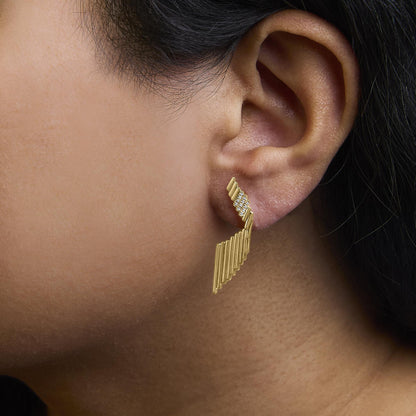 Close-up side view of a yellow metal earring with white round gemstones in prong settings, worn on a model's ear.
