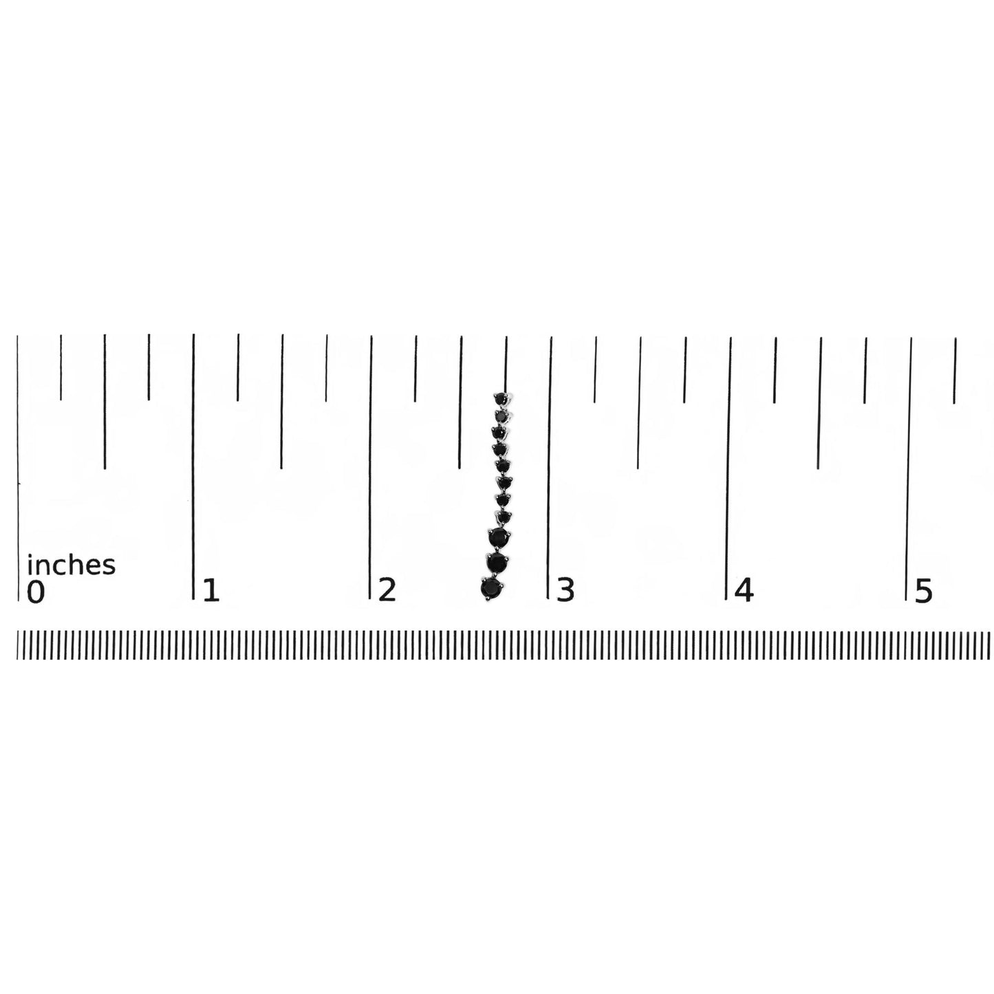 Close-up front view of a white metal earring with multiple round black gemstones in prong settings, placed vertically on a ruler for size reference.