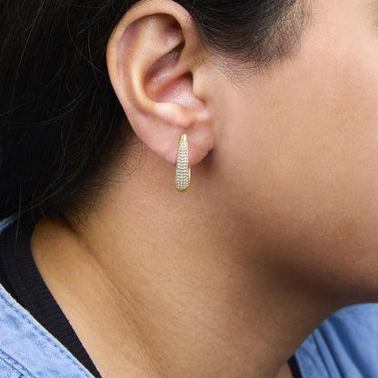 Close-up side view of a yellow metal earring with pave-set round white gemstones, worn on a model's ear.